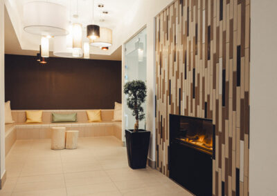 Kaminlounge im Spa mit moderner Wandverkleidung in Holzoptik, Kunstfeuer und Dekoration – Innenraum für entspannte Gespräche oder Lesepausen.