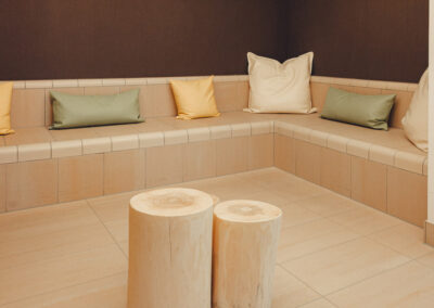 Nische mit Sitzpolstern in Beige und Grün, Holztisch und Pflanzen – ruhiger, barrierefreier Warte- oder Gesprächsbereich.