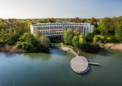 Weitblick von leicht schräg oben von oben auf die Hotelanlage mit See und Bootssteg.
