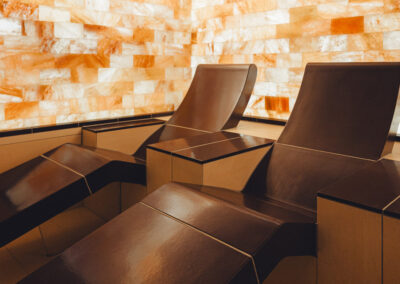 Liegen vor beleuchteter Salzwand aus Naturstein, umgeben von ruhigen Lichtfarben – Raum mit therapeutischem Ambiente.