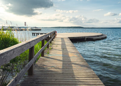 Holzsteg in den See mit Plattform, Schilfgras am Rand.