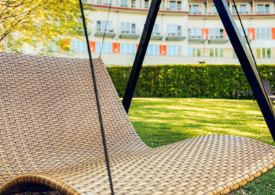 Freistehende Holzschaukel mit Liegefunktion im gepflegten Garten vor dem Hotelgebäude – Sitz- und Liegegelegenheit im Außenbereich.