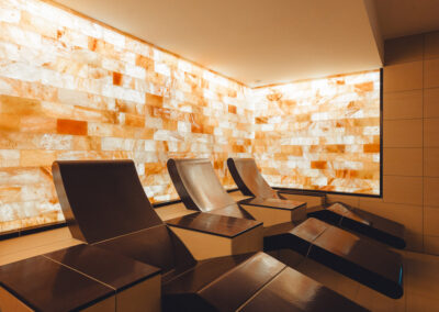 Liegen vor beleuchteter Salzwand aus Naturstein, umgeben von ruhigen Lichtfarben – Raum mit therapeutischem Ambiente.