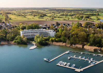 Weitblick von leicht schräg oben von oben auf die Hotelanlage mit See und Bootssteg.