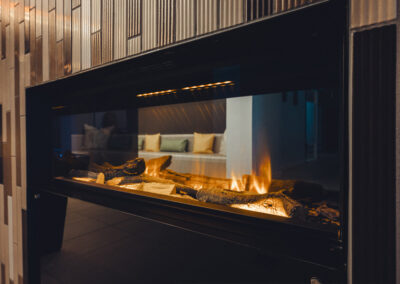 Kaminlounge im Spa mit moderner Wandverkleidung in Holzoptik, Kunstfeuer und Dekoration – Innenraum für entspannte Gespräche oder Lesepausen.