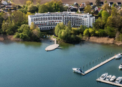 Weitblick von leicht schräg oben von oben auf die Hotelanlage mit See und Bootssteg.