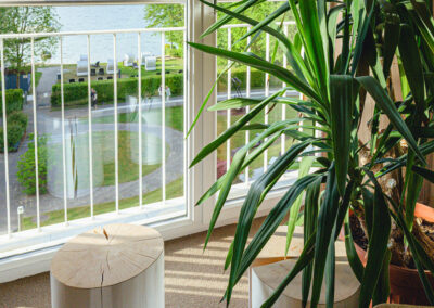 Gemütliche Leseecke mit Polstersessel, Regal mit Büchern und Dekoobjekten, stilvolle Raumbeleuchtung, Fenster mit Blick auf Natur, geeignet als ruhiger Rückzugsort.